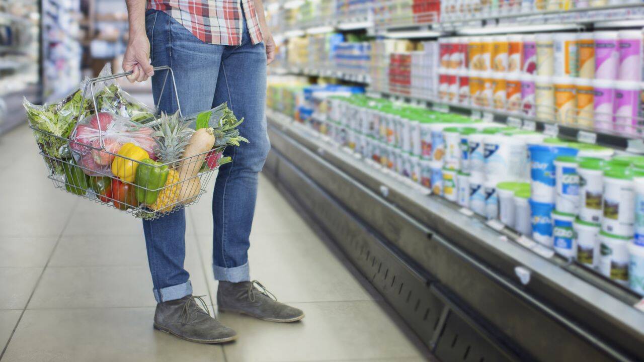 o persoana in fata unui raft cu lactate care tine un cos cu cumparaturi in mana